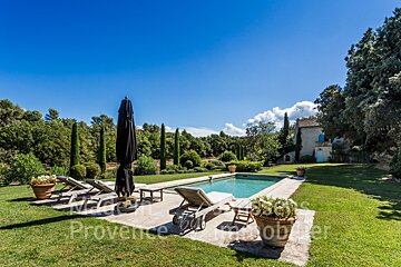 A large swimming pool is surrounded by lawn chairs and umbrellas and the word provence is on the lawn