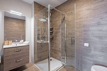 Modern bathroom featuring wood-look tiled walls, a glass shower stall, a wooden vanity with sink, and a large mirror.