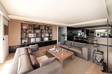 A modern open-plan living room with gray sofas, a wooden coffee table, and built-in shelves, connected to a dark, contemporary kitchen.