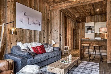 A cozy, rustic wood-paneled living room and kitchen area with a sofa, block coffee table, and polar bear art on the wall.