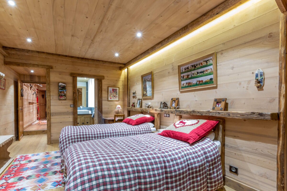 Rustic wooden bedroom with two twin beds featuring red and white plaid bedding under a warm wood-paneled ceiling.