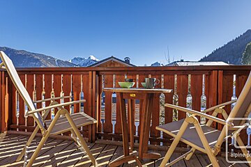 Two chairs and a table on a balcony with a mountain in the background