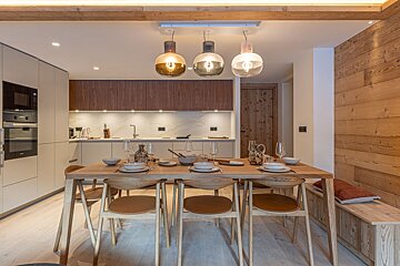 Chic, modern kitchen & dining area with a wooden table set for guests, stylish pendant lights, built-in appliances, and warm wood accents.