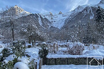A serene winter scene with snow-laden trees and shrubs in the foreground, leading to majestic, snow-capped mountains under a clear sky.