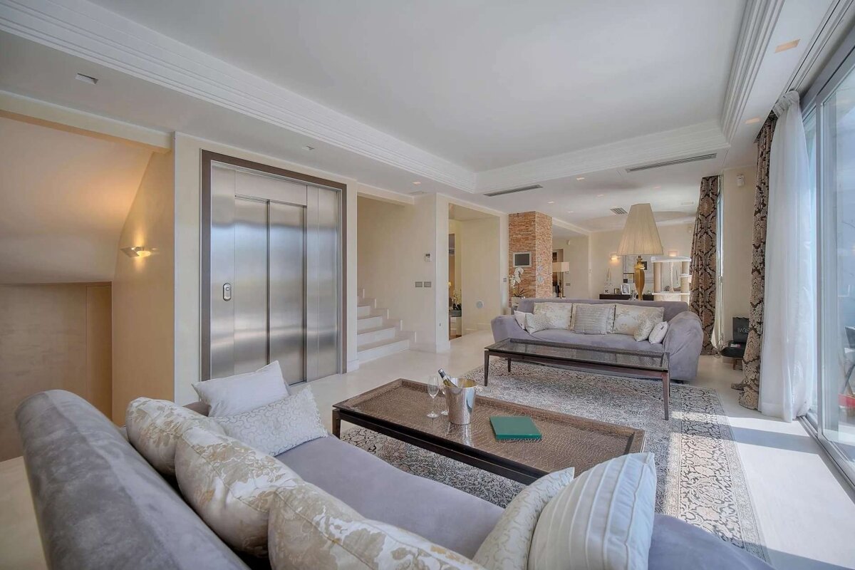 Elegant, spacious living room with a modern elevator, plush sofas, a coffee table, and large glass doors leading outdoors.