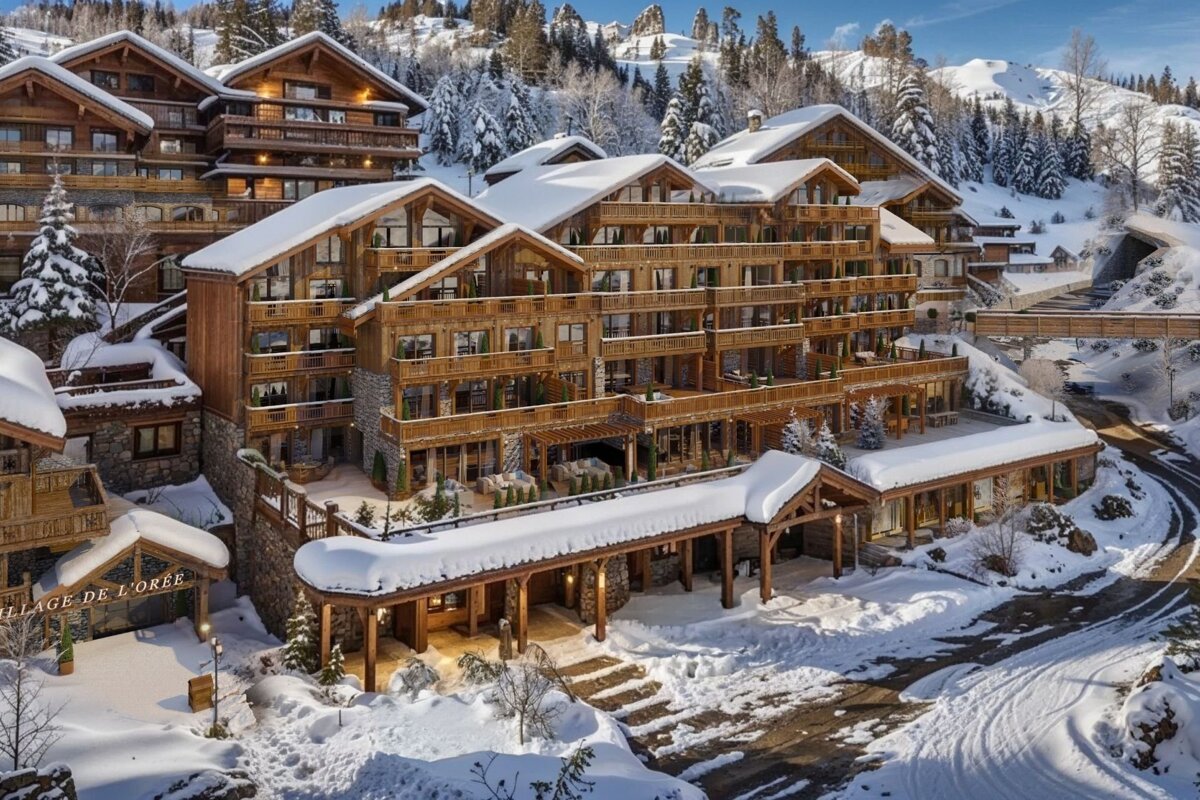 Stunning multi-story wooden chalets and a hotel blanketed in fresh snow, nestled in a sunny, forested winter mountain resort.