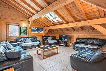 Rustic wooden chalet living room featuring vaulted beamed ceilings, a skylight, several black leather sofas, and a central coffee table.