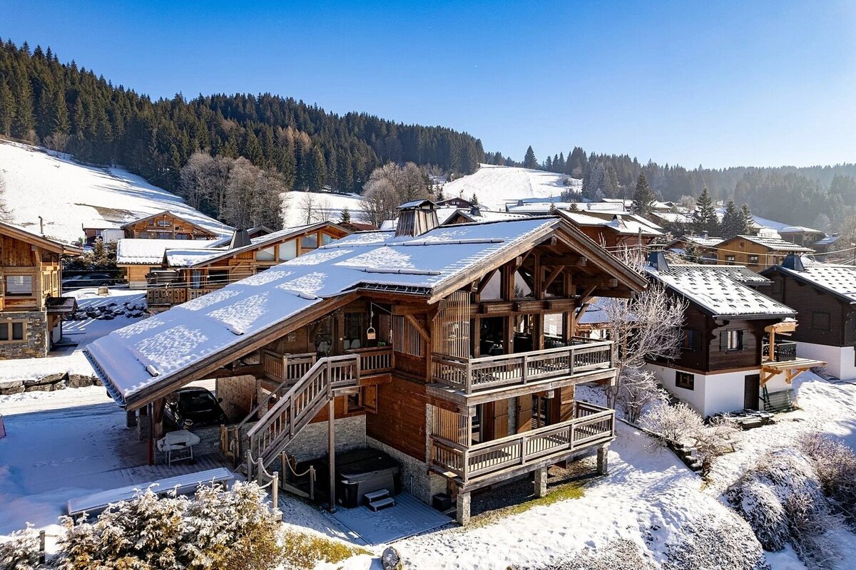 Snow-capped wooden chalets in a sunny alpine ski village, surrounded by pine forests under a clear blue sky.
