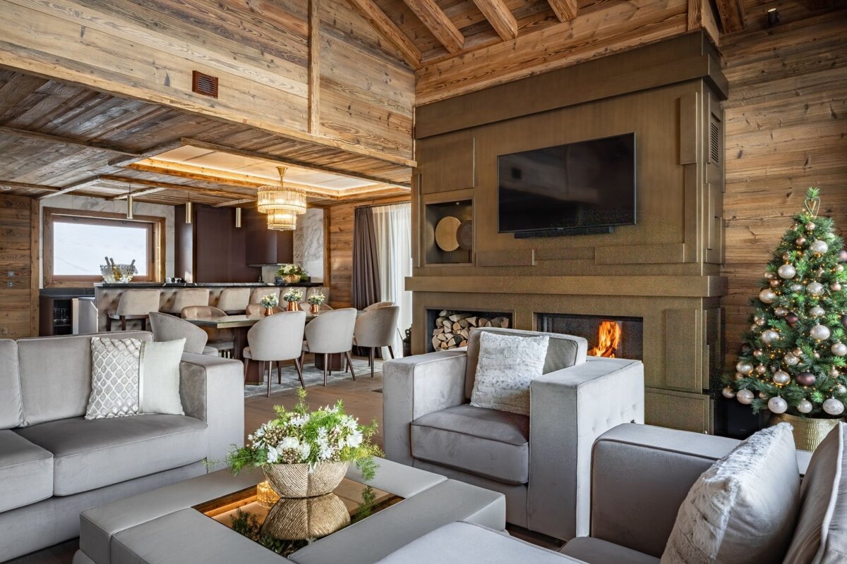 Luxurious, open-plan wooden chalet interior with a cozy living area, fireplace, TV, dining space, and a festive Christmas tree.