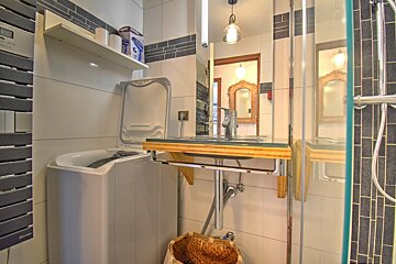 A small bathroom with a top-loading washing machine next to a modern floating wooden vanity, mirror, and glass-enclosed shower.