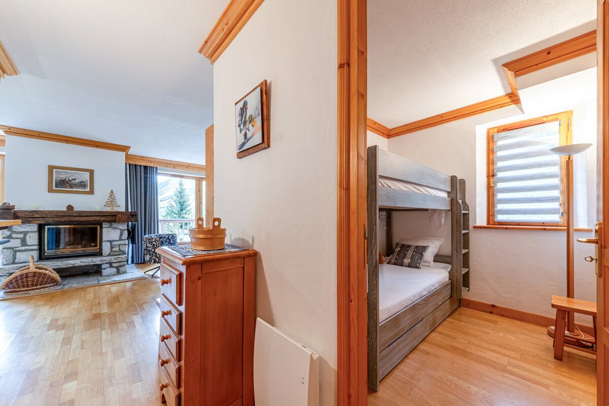 Cozy cabin interior showing a living room with a stone fireplace and a separate small bunk bed room, all featuring warm wooden accents.