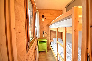 A small, wood-paneled bedroom featuring a wooden bunk bed with white linens and a bright green bedside table.