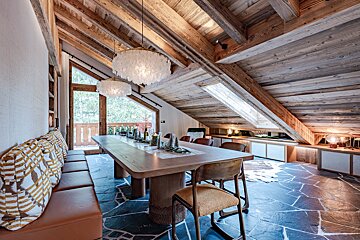Cozy chalet dining room featuring a vaulted wood ceiling, flagstone floor, a long wooden table, and two fluffy white pendant lights.