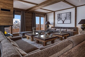 A warm, elegant chalet living room featuring a fireplace, comfy sofas, deer decor, and incredible snowy mountain vistas.