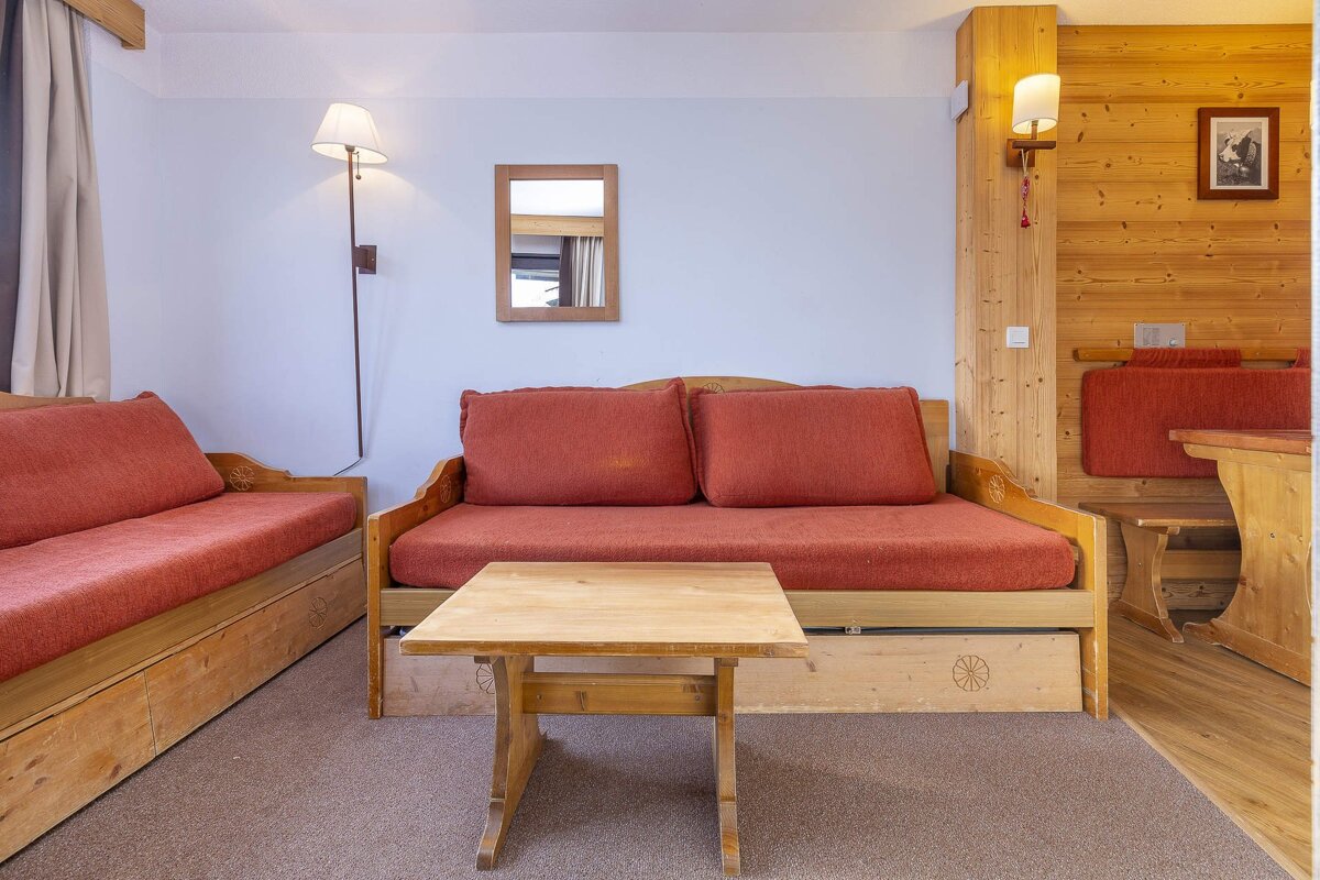 A cozy room with two wooden daybeds with red cushions, a wooden coffee table, and mixed wall finishes of light blue and wood paneling, featuring a dining nook.