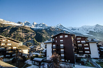A view of a snowy mountain range with a few buildings in the foreground
