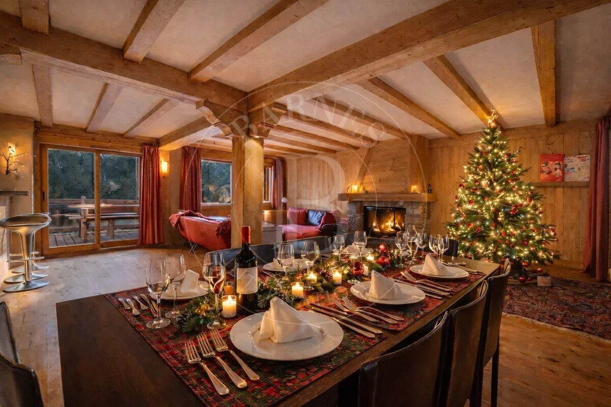 A cozy, festive chalet living room with a lit Christmas tree, dining table set for dinner, and a fireplace.