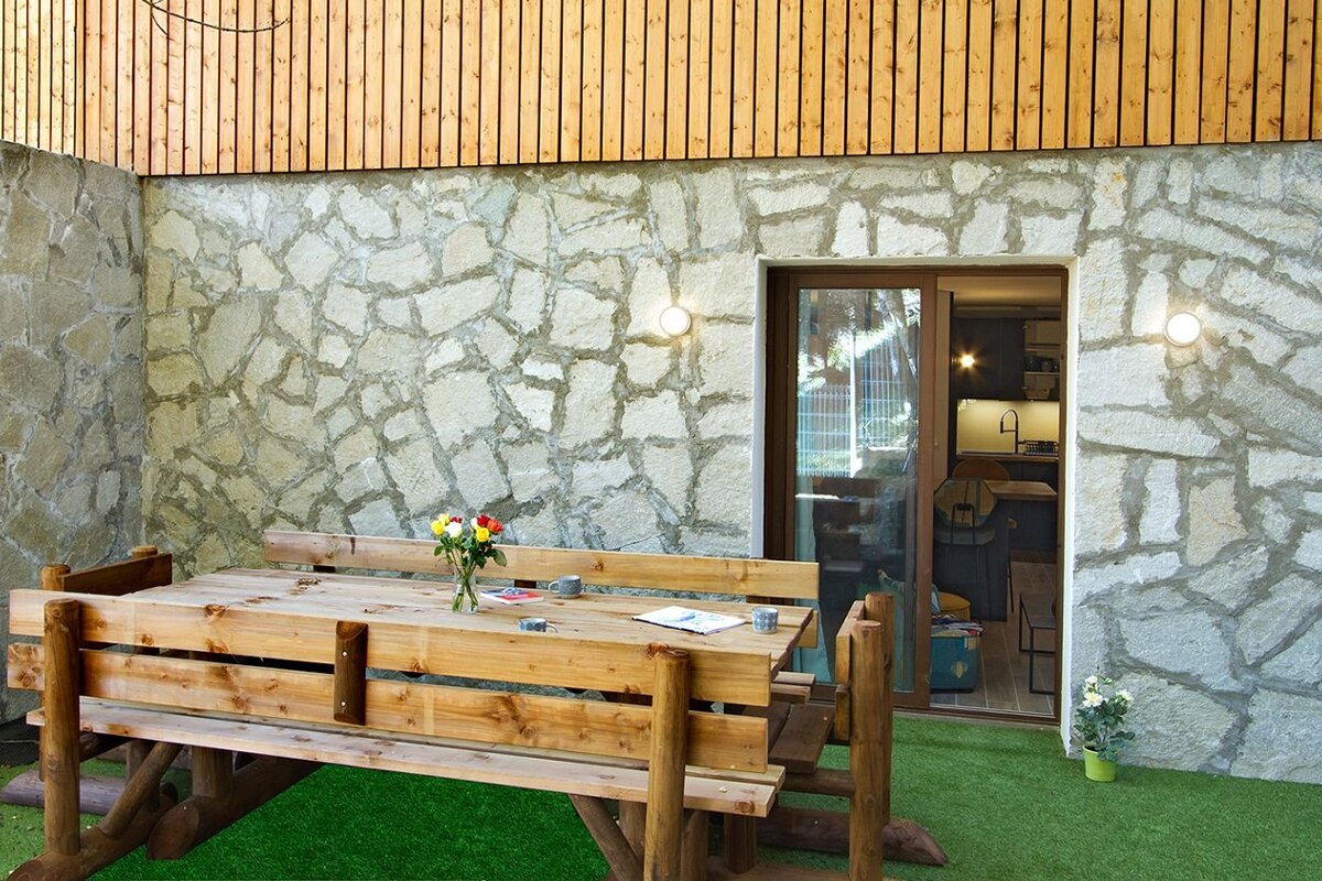 A wooden table with a vase of flowers on it in front of a stone wall