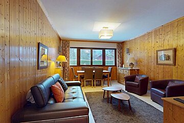 Cozy wood-paneled living/dining room with dark leather seating, a wooden dining table, and a large window offering natural light.