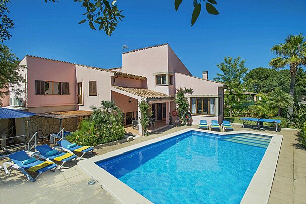 A large pink house with a large swimming pool in front of it