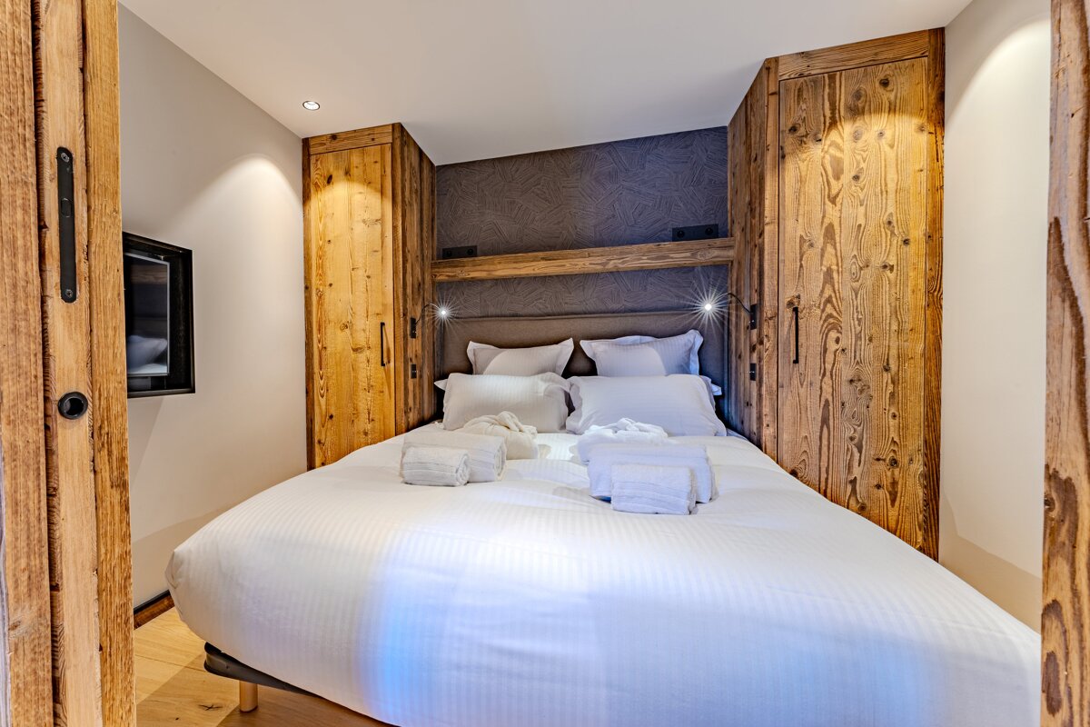 Cozy chalet bedroom featuring a double bed with white linens flanked by built-in rustic wooden closets.