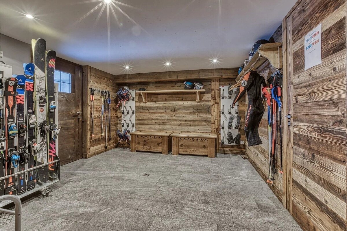A rustic wooden ski room featuring storage racks, benches, skis, and gear with stone-tile flooring.