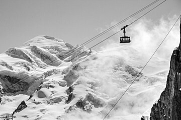 A black and white photo of a ski lift going up a snowy mountain