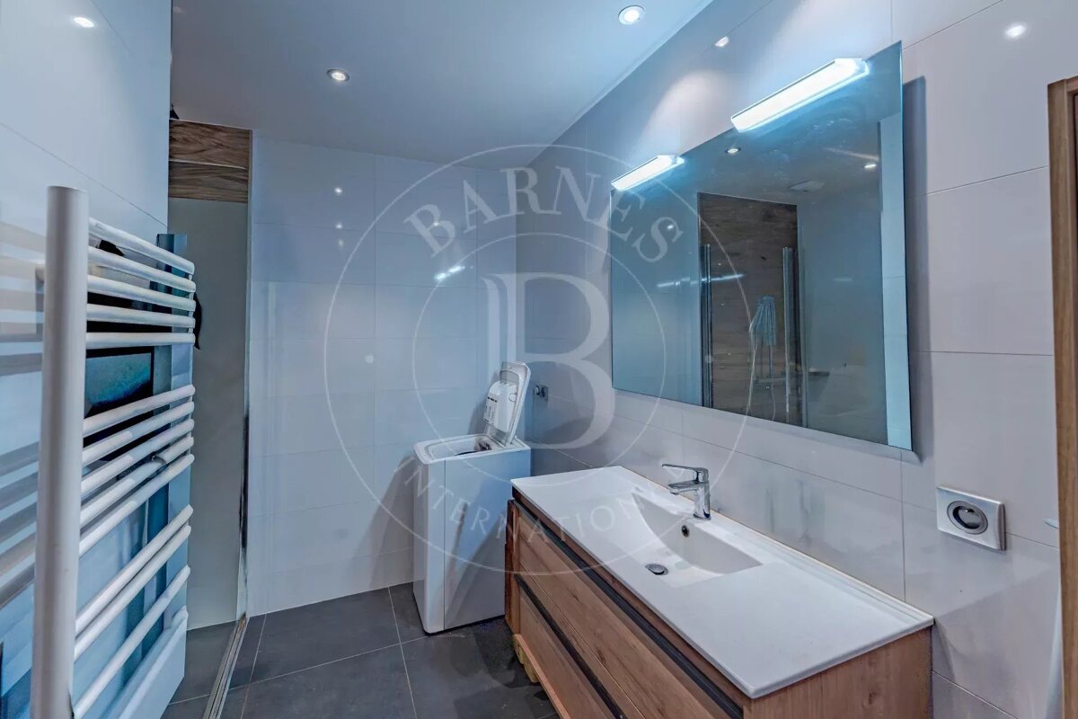 Modern bathroom featuring a wooden vanity, a large mirror with integrated lights, and a top-loading washing machine.