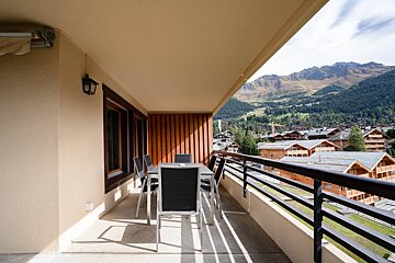 A balcony with a table and chairs and mountains in the background