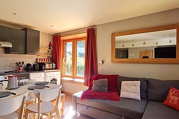 Cozy studio apartment featuring a grey sofa with red accents, a large wooden mirror, and a small adjacent kitchen area.
