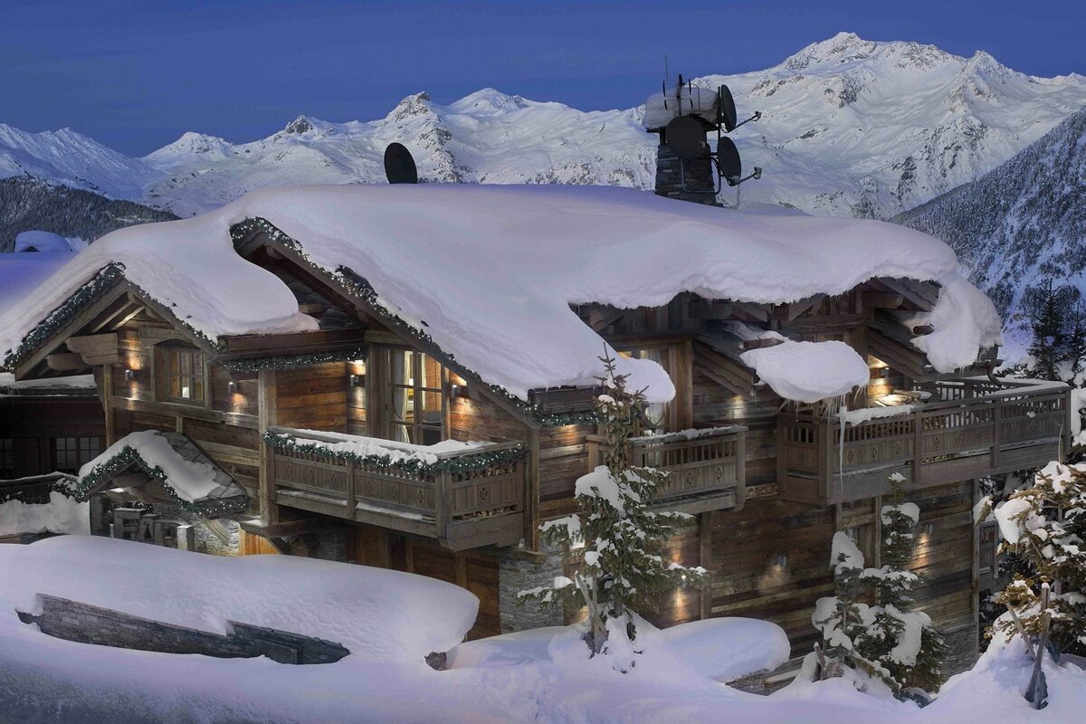 A snow covered house with mountains in the background