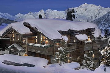 A luxurious wooden chalet blanketed in deep snow, nestled among snowy mountains under a twilight sky, with warm lights and satellite dishes.
