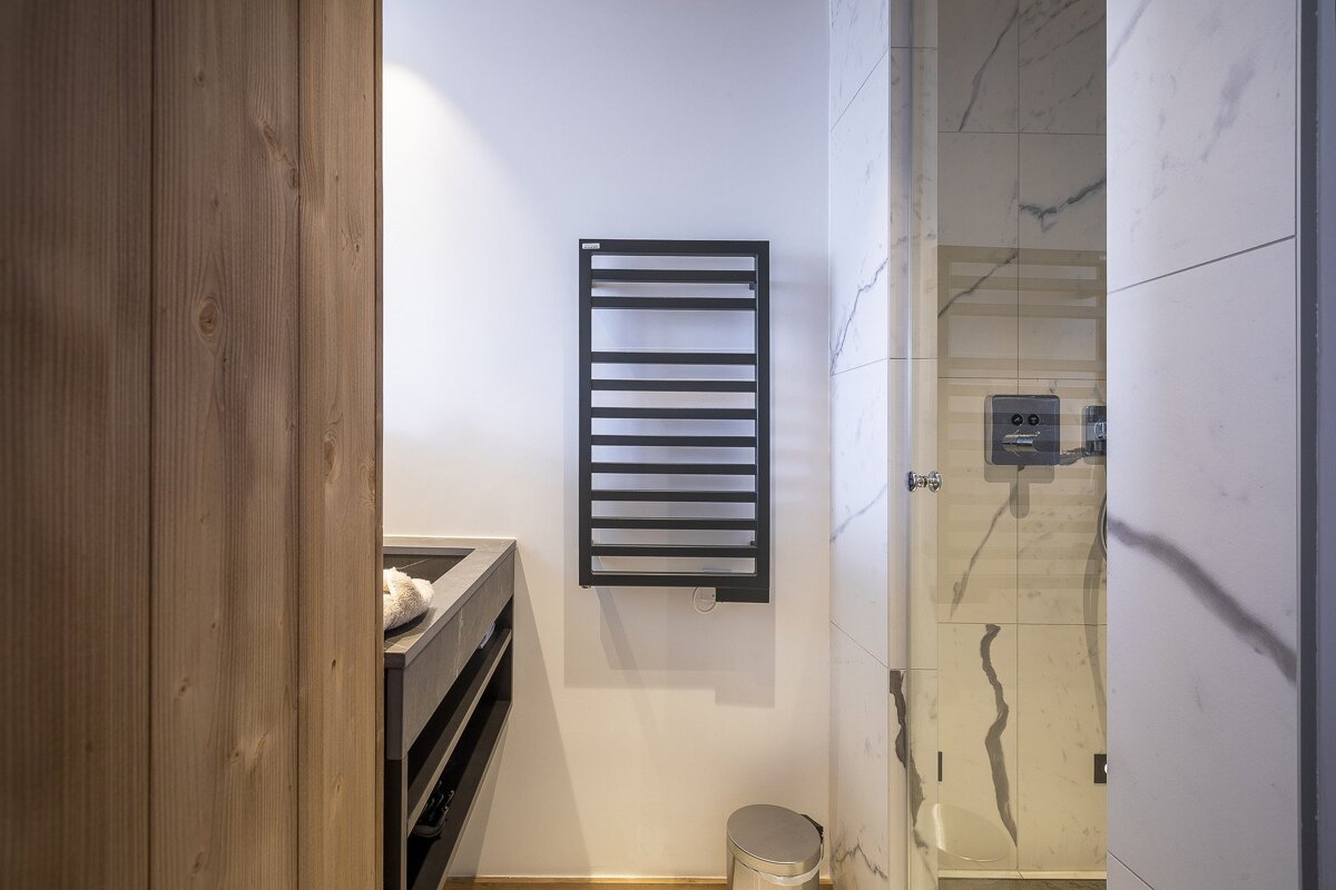 Modern bathroom featuring a black heated towel rack on a white wall, a dark vanity, and a marble-tiled shower.