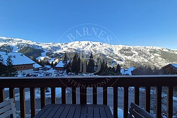 Panoramic view from a balcony of snow-covered mountains with ski slopes, pine trees, and chalets under a clear blue sky.