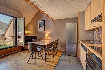 Cozy alpine apartment featuring a kitchen, dining area, and open balcony door overlooking mountains.