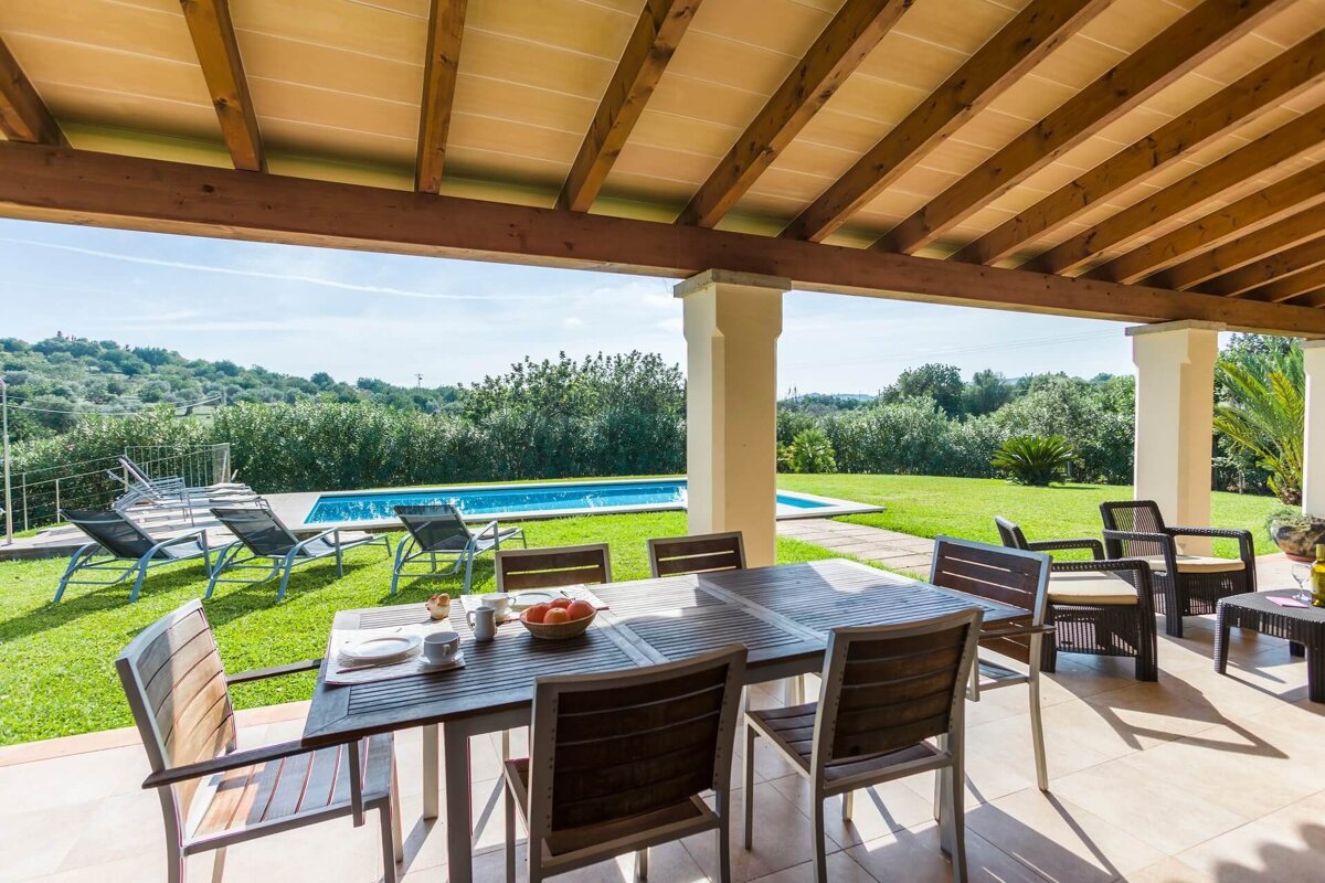A patio with a table and chairs and a pool in the background