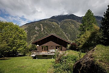 A house with a mountain in the background is surrounded by trees