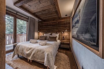 Rustic wooden bedroom with a cozy bed, balcony overlooking snowy trees, and a large mountain-themed artwork. Warm and inviting atmosphere.