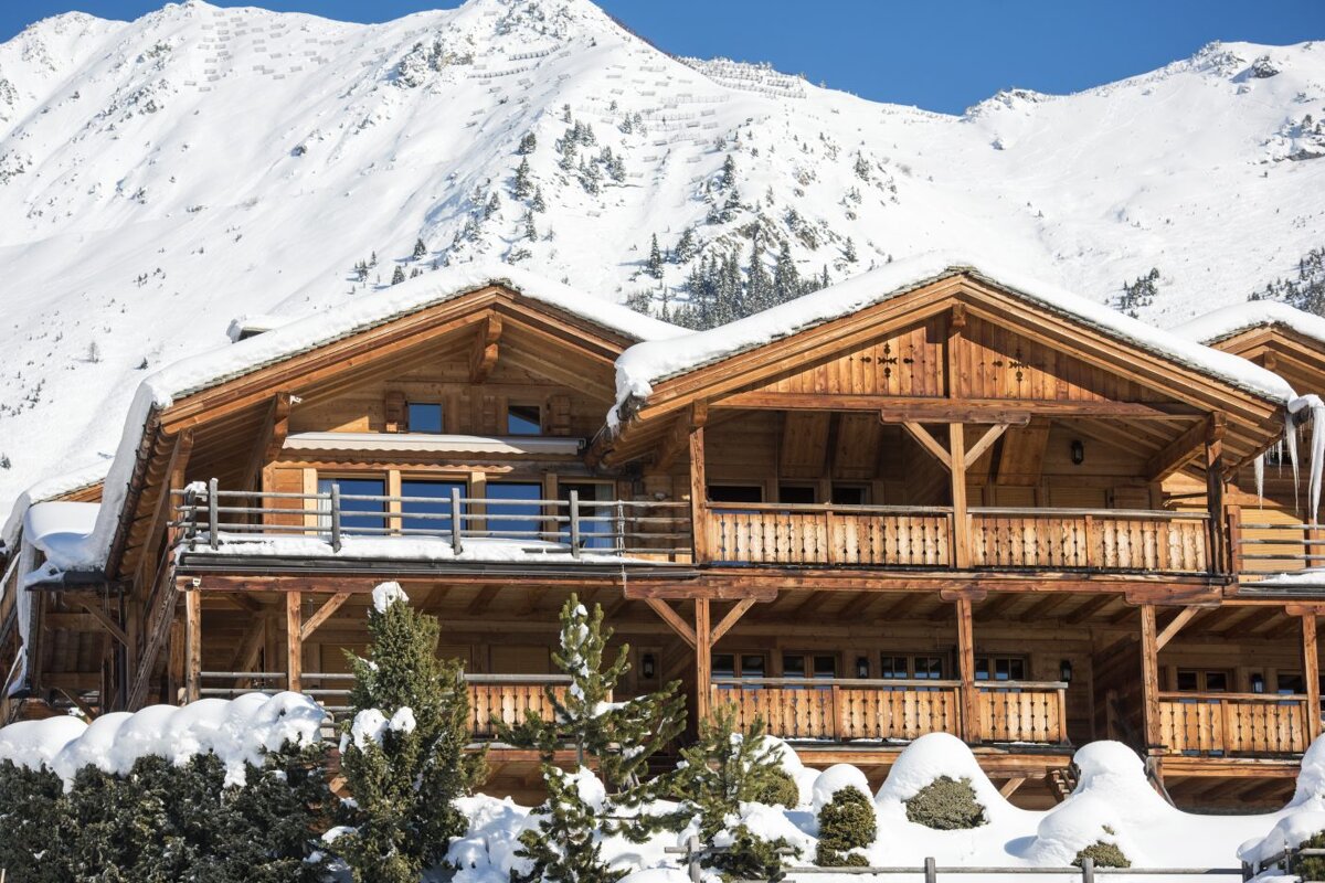 A large wooden house in the snow with a mountain in the background