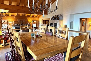 Rustic wooden dining table and chairs with cushions under a metal chandelier in a cozy chalet.