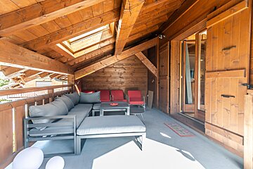 A wooden balcony with a couch and chairs and a rug that says welcome
