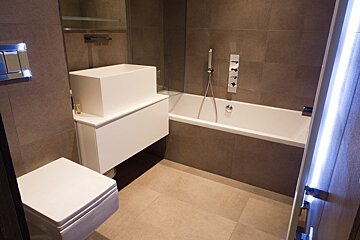 Modern bathroom with a sleek white vanity, sink, bathtub, and toilet set against minimalist grey-brown tiles.