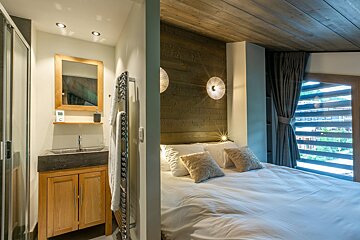 Cozy chalet bedroom with wooden accents and a white bed, adjacent to an ensuite bathroom with a wooden vanity.
