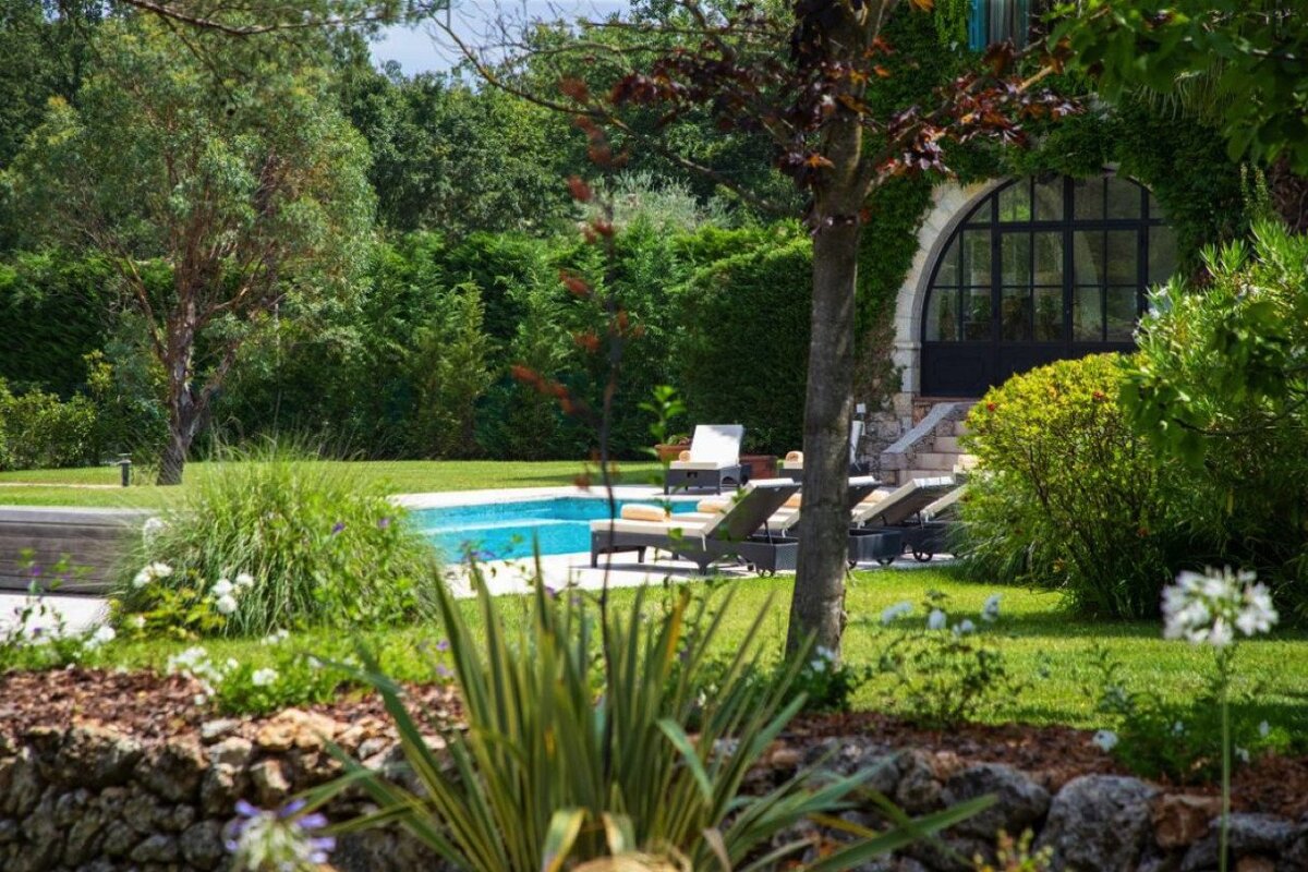 A large swimming pool is surrounded by lawn chairs and trees
