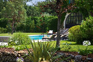 A large swimming pool is surrounded by lawn chairs and trees