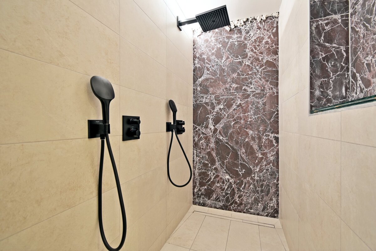 A bathroom with two shower heads and a marble wall