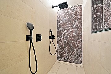 A bathroom with two shower heads and a marble wall