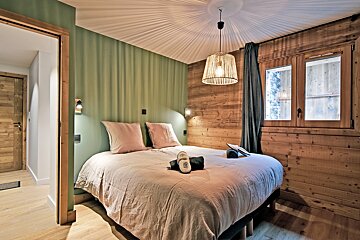 Cozy cabin-style bedroom with a green accent wall, wood paneling, a double bed, and a woven pendant light casting shadows on the ceiling.