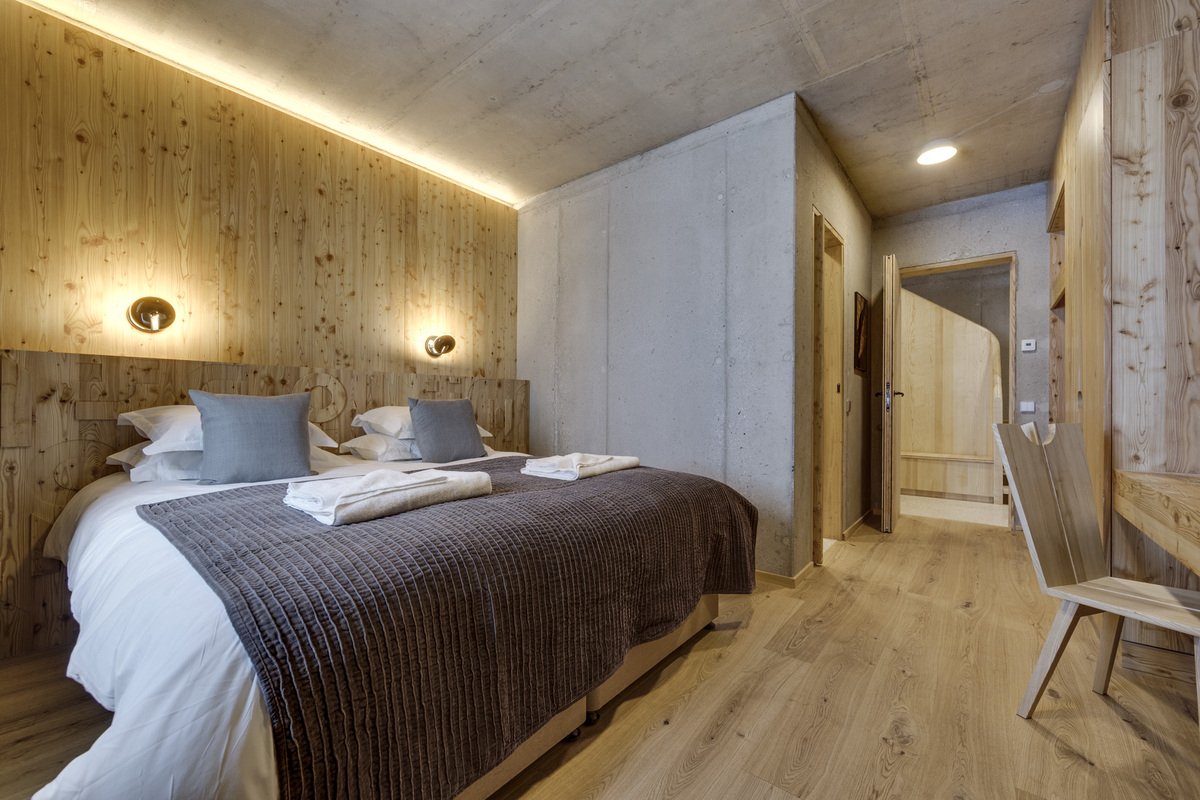 Modern bedroom combining raw concrete and warm wood paneling, featuring a cozy double bed and minimalist wooden furniture.