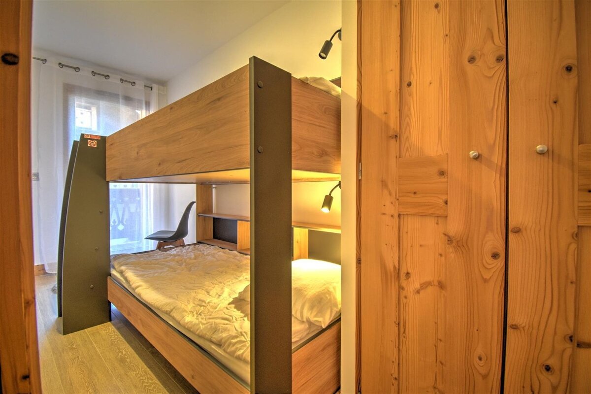 Modern wooden bunk beds with integrated lighting in a cozy bedroom, featuring a window and warm wooden wardrobe panels.